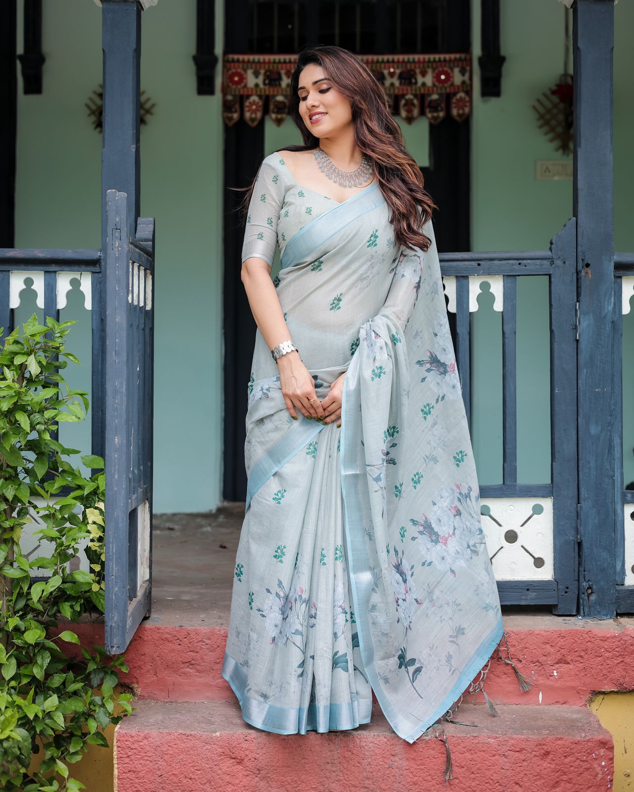 Light pastel blue linen saree with floral print, tassels on the edges, and an attached matching blouse piece.